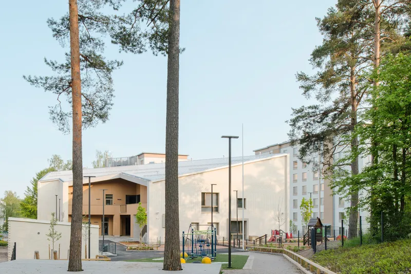 Pale metal-clad volumes with a central courtyard seen through tall pine trees at dusk