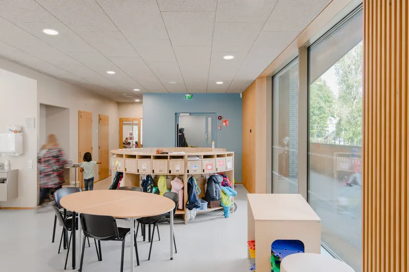 Classroom interior with blue accent wall, storage cubbies, round tables and a timber slat screen