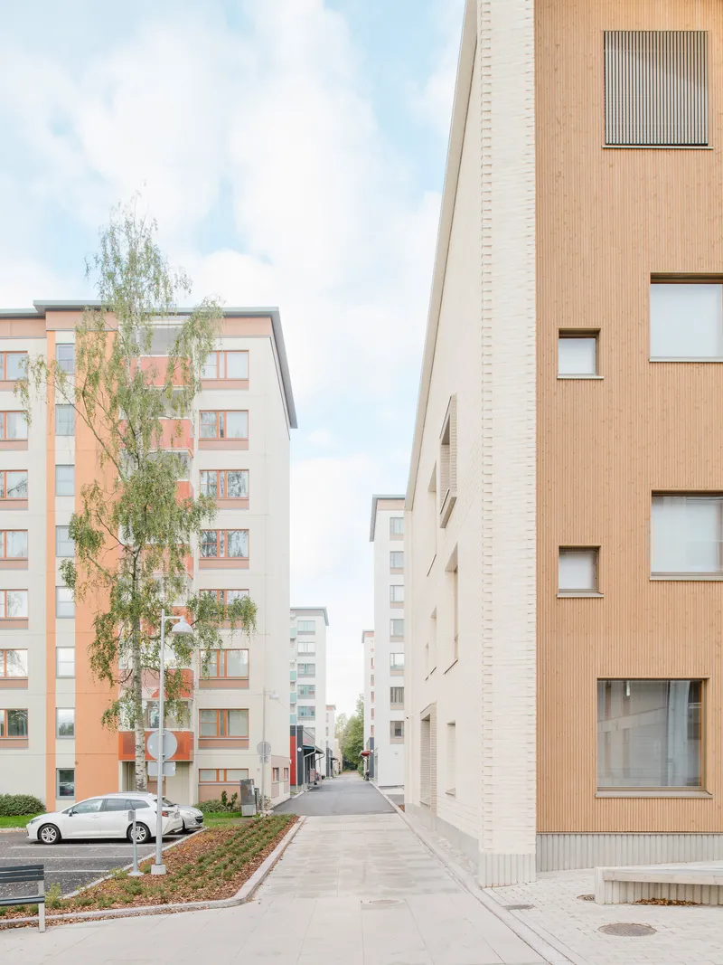 Pedestrian street between brick-clad residential blocks with young trees and parked cars