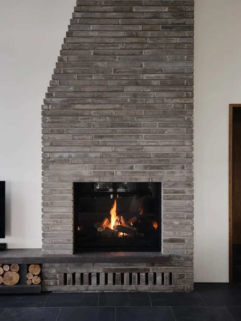 Tapered grey brick fireplace chimney rising from floor to ceiling with an active fire below