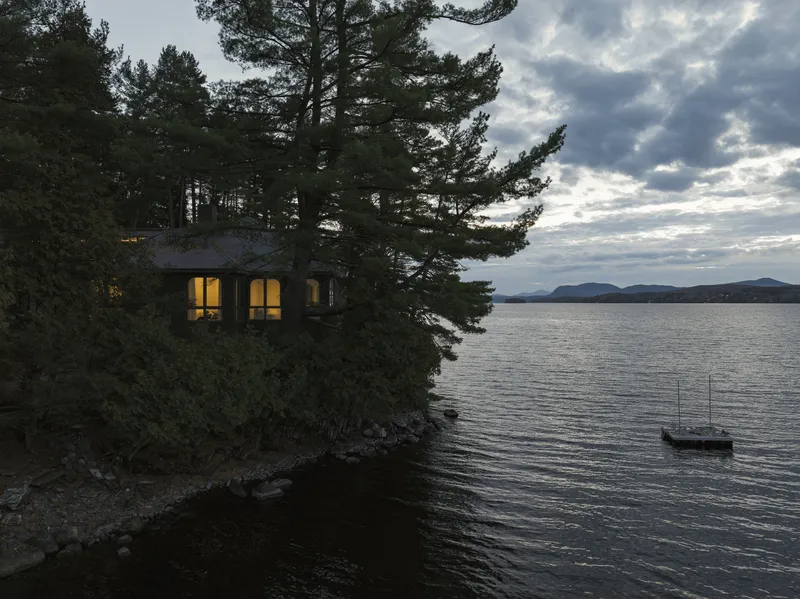 Lakeside view of the residence perched on rocky shore with a sailboat moored nearby