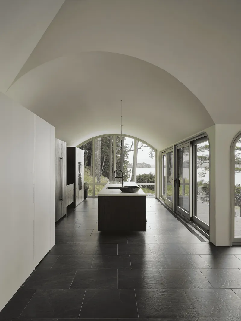 Vaulted kitchen with dark stone floor and arched glazing overlooking the lake