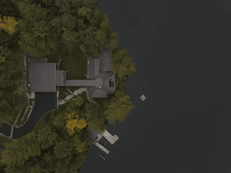 Drone view of the compound on the wooded shoreline with dock in dark water