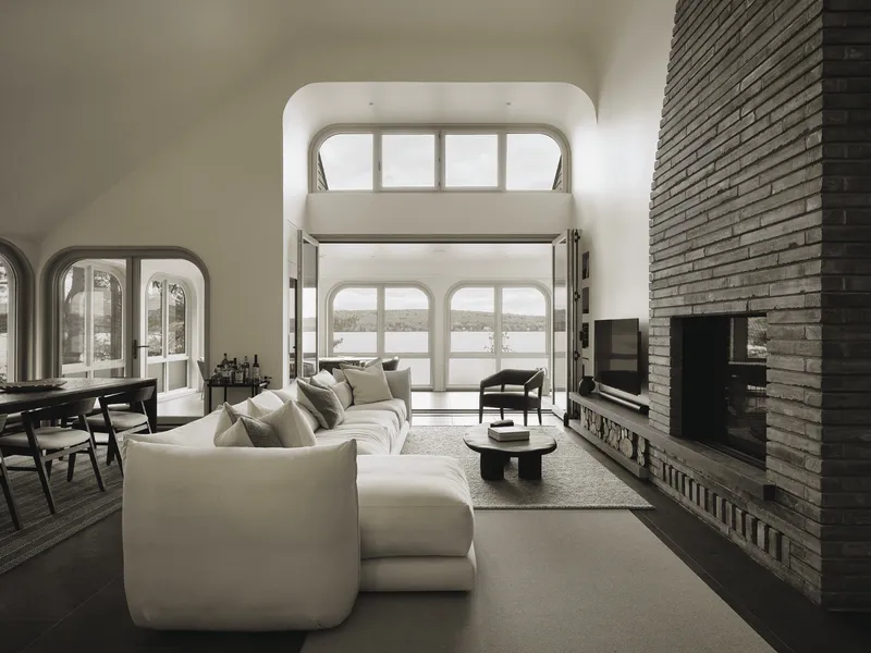 Double-height living space with arched window wall, stacked brick fireplace chimney, and lake view beyond