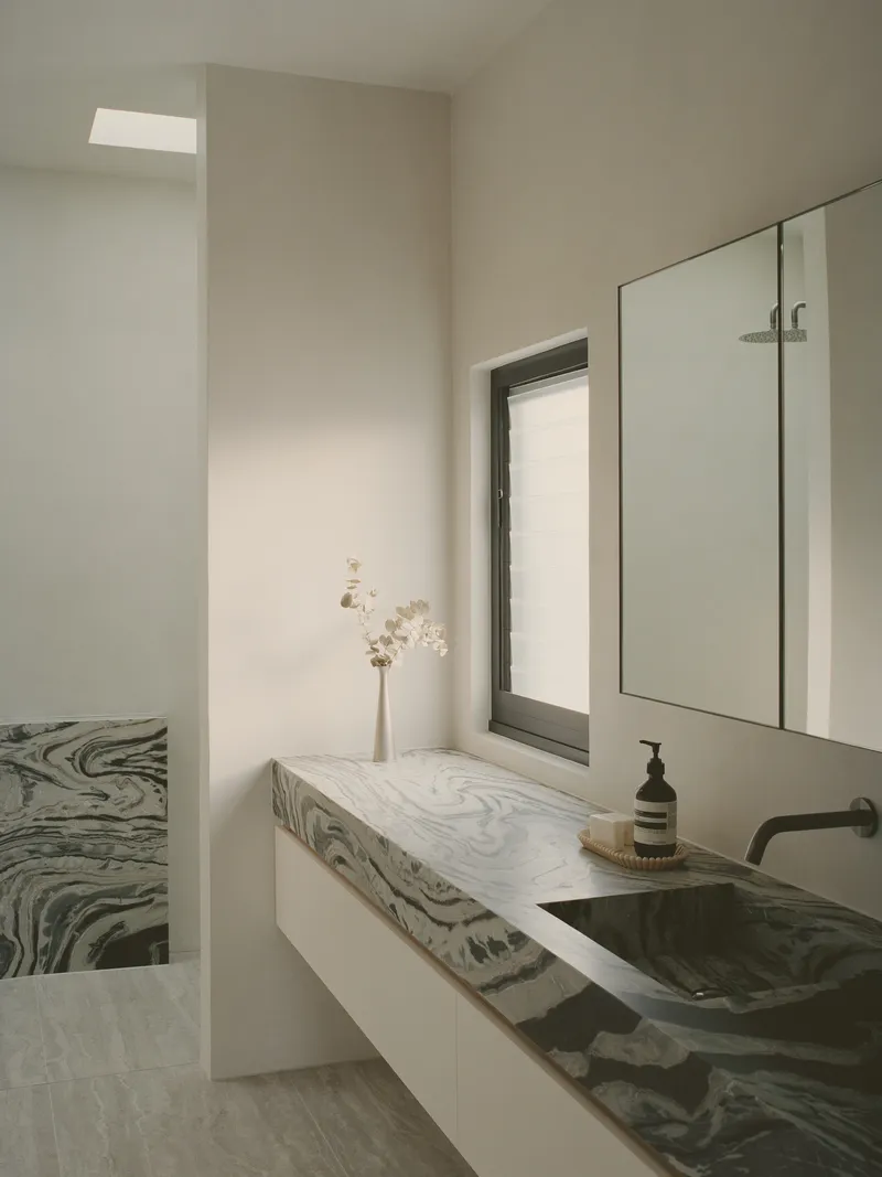 Bathroom vanity with swirled grey marble countertop and integrated basin under soft skylight illumination