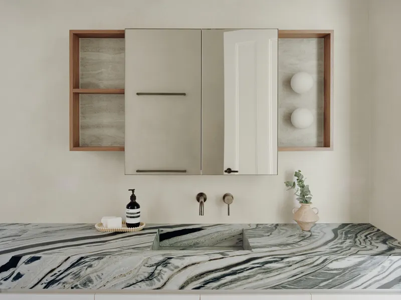 Marble vanity with integrated sink below timber-framed mirror cabinet and wall-mounted brass fixtures