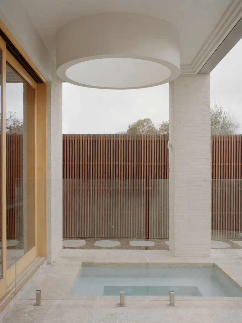 Sunken bathtub beneath cylindrical skylight opening to courtyard with vertical timber screening and brick column
