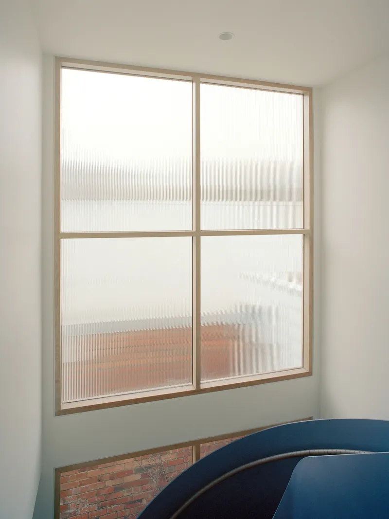 Timber-framed window with translucent reeded glass overlooking a brick terrace in soft daylight