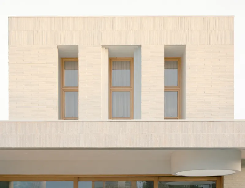 Facade detail showing three tall timber-framed windows set into pale brick wall with vertical bond