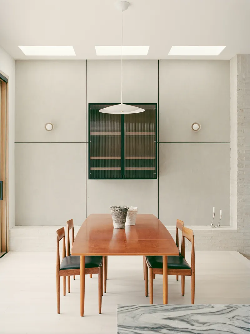 Dining room with timber table and green upholstered chairs below three skylights and pendant light fixture