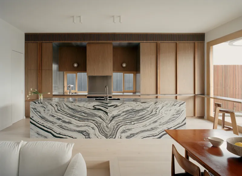 Kitchen island clad in swirling grey and white marble below timber cabinetry and mirrored splashback panels