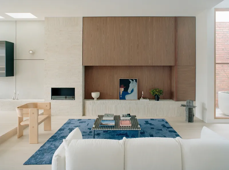 Living area with blue patterned rug, white painted brick fireplace, and timber entertainment joinery under skylight