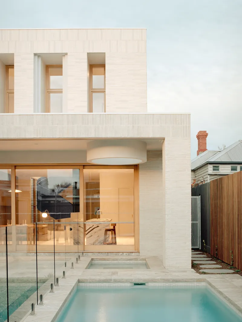 Rear courtyard with rectangular pool and pale brick facade overlooking an adjacent timber fence