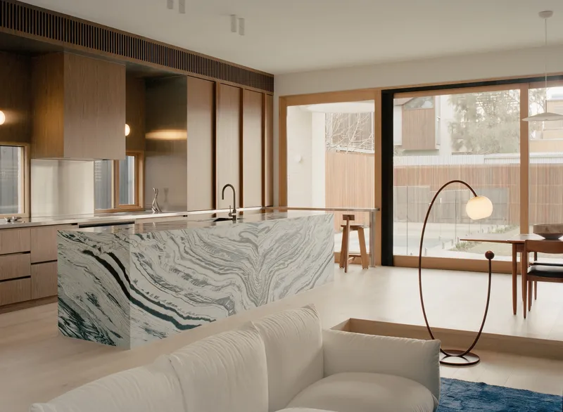 Kitchen island clad in swirled grey marble beneath timber cabinetry and sliding screens