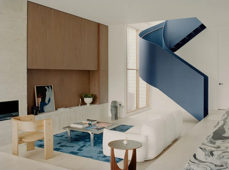 Blue folded metal staircase ascending through a double-height living space with timber joinery