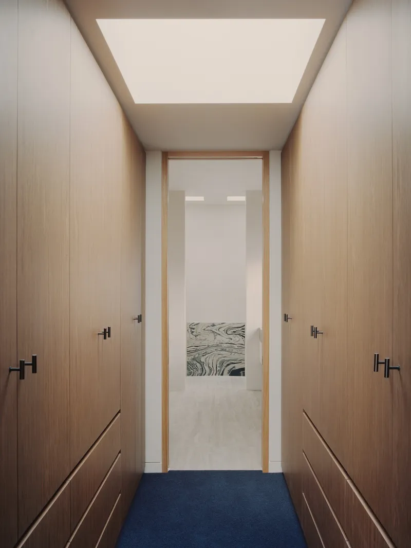 Narrow dressing corridor with timber wardrobes flanking a doorway framed by large ceiling skylight
