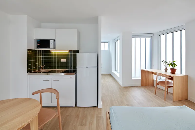 Studio unit with kitchenette featuring dark green tile backsplash and light wood flooring throughout