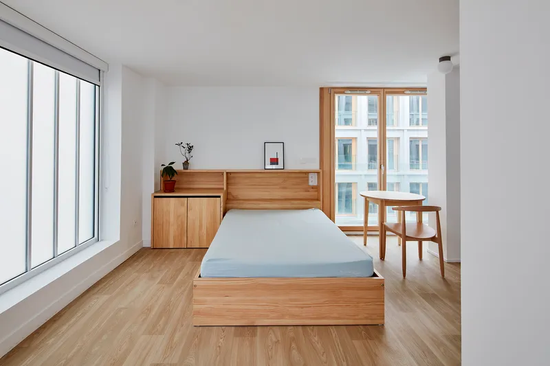 Bedroom with timber platform bed and built-in headboard storage overlooking the courtyard through large windows