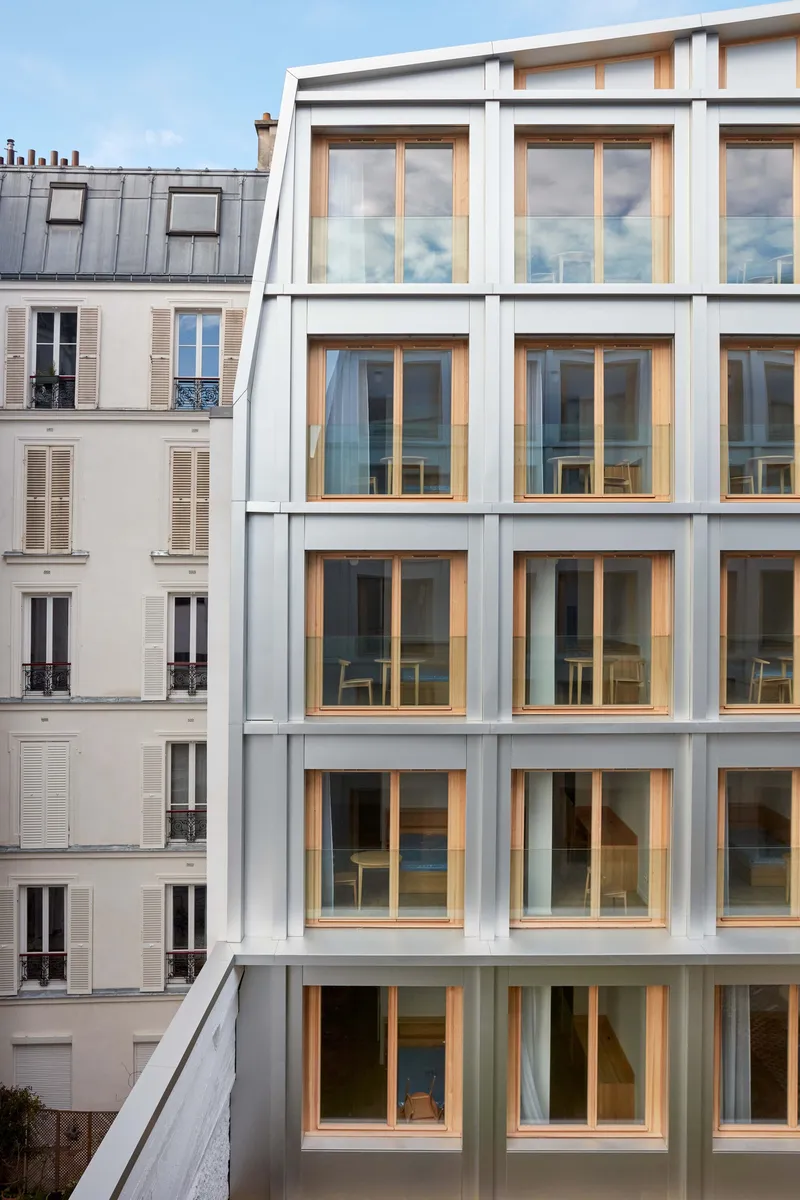 Rear facade with stacked timber-framed windows overlooking adjacent residential buildings at dusk