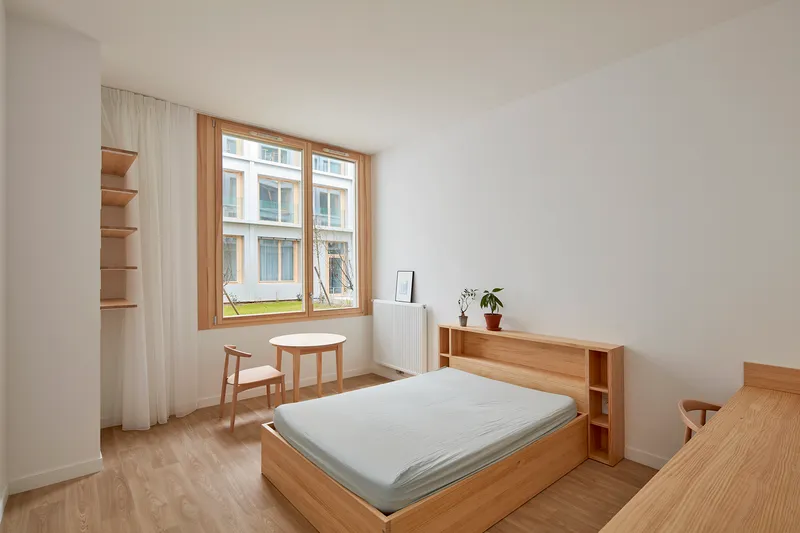 Bedroom with timber bed frame and open shelving beside a timber-framed window overlooking a courtyard