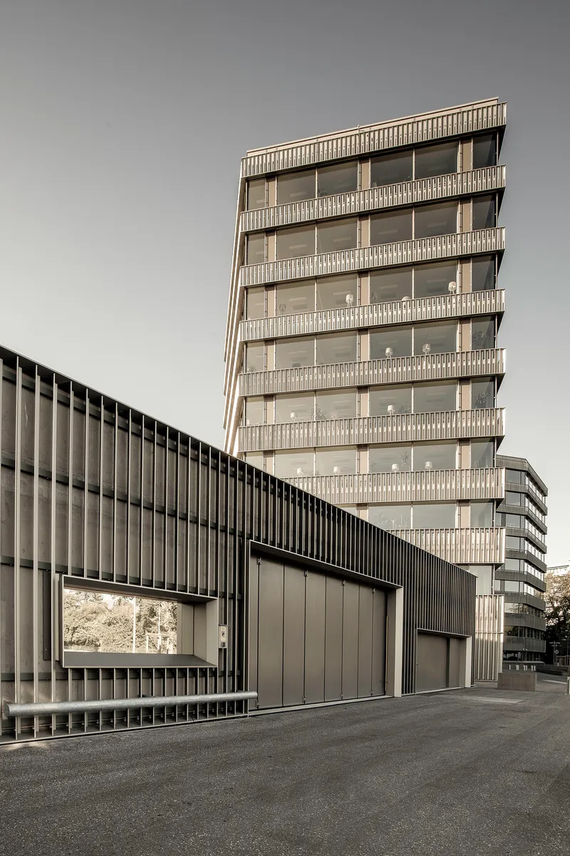 Vertical louvered tower behind a dark ribbed garage volume with metal gates