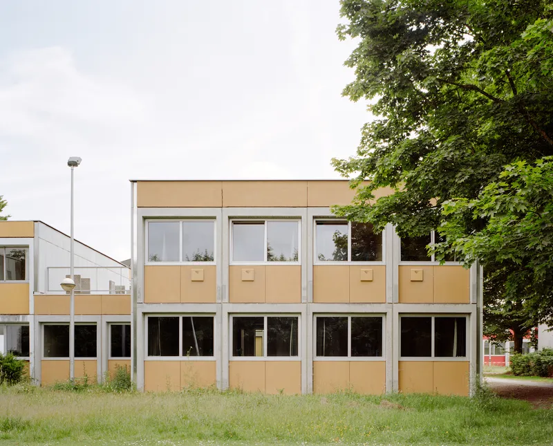Street facade with orange panel infill, white frames and floor-to-ceiling glazing beneath summer trees
