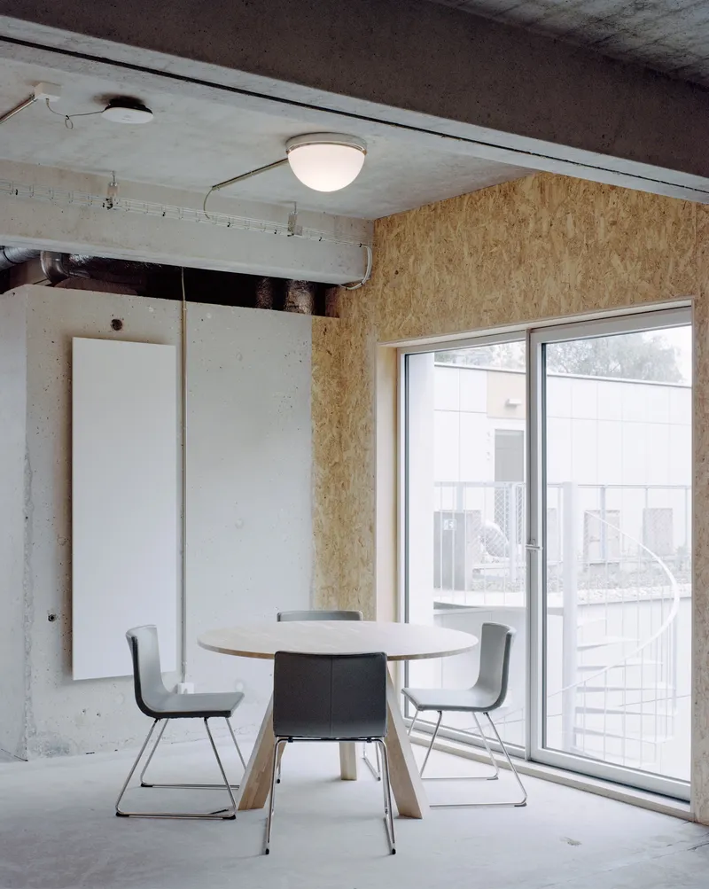 Dining area with round table, exposed concrete ceiling, oriented strand board wall and sliding door to balcony