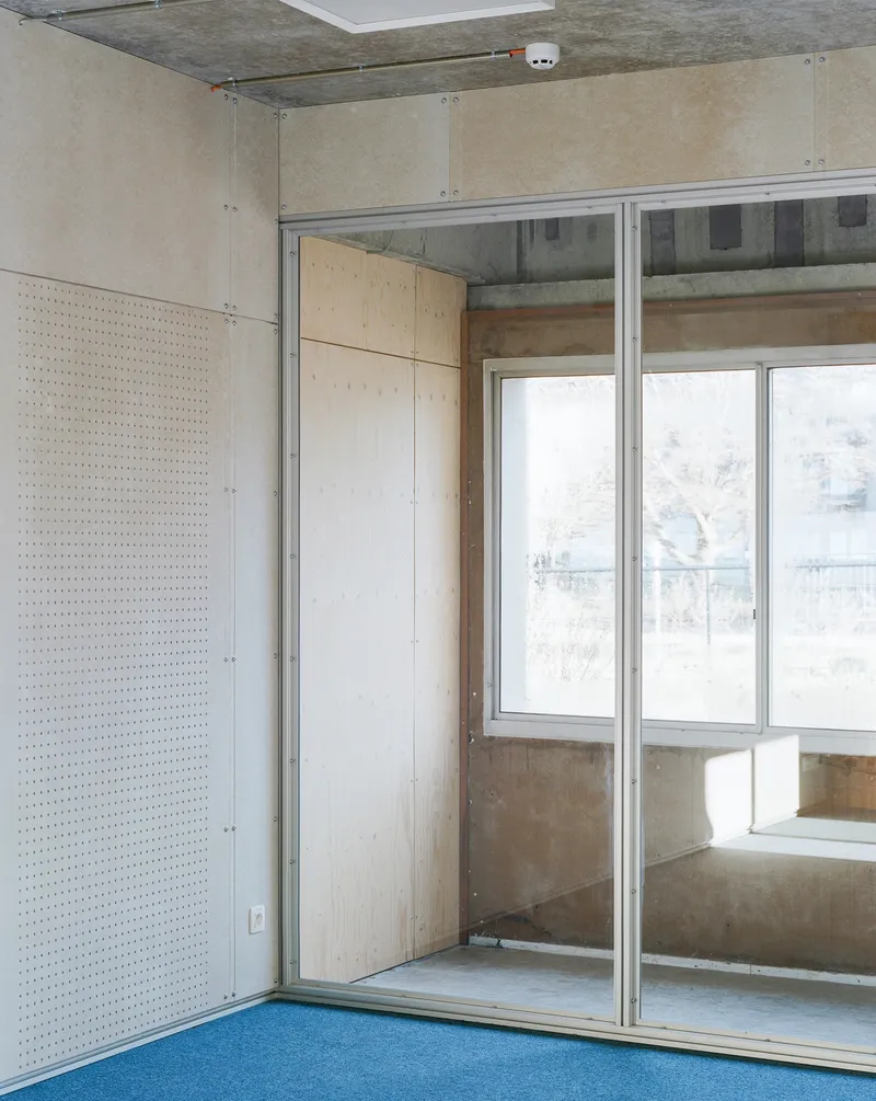 Corner interior with perforated plywood wall panel and sliding glass door to balcony