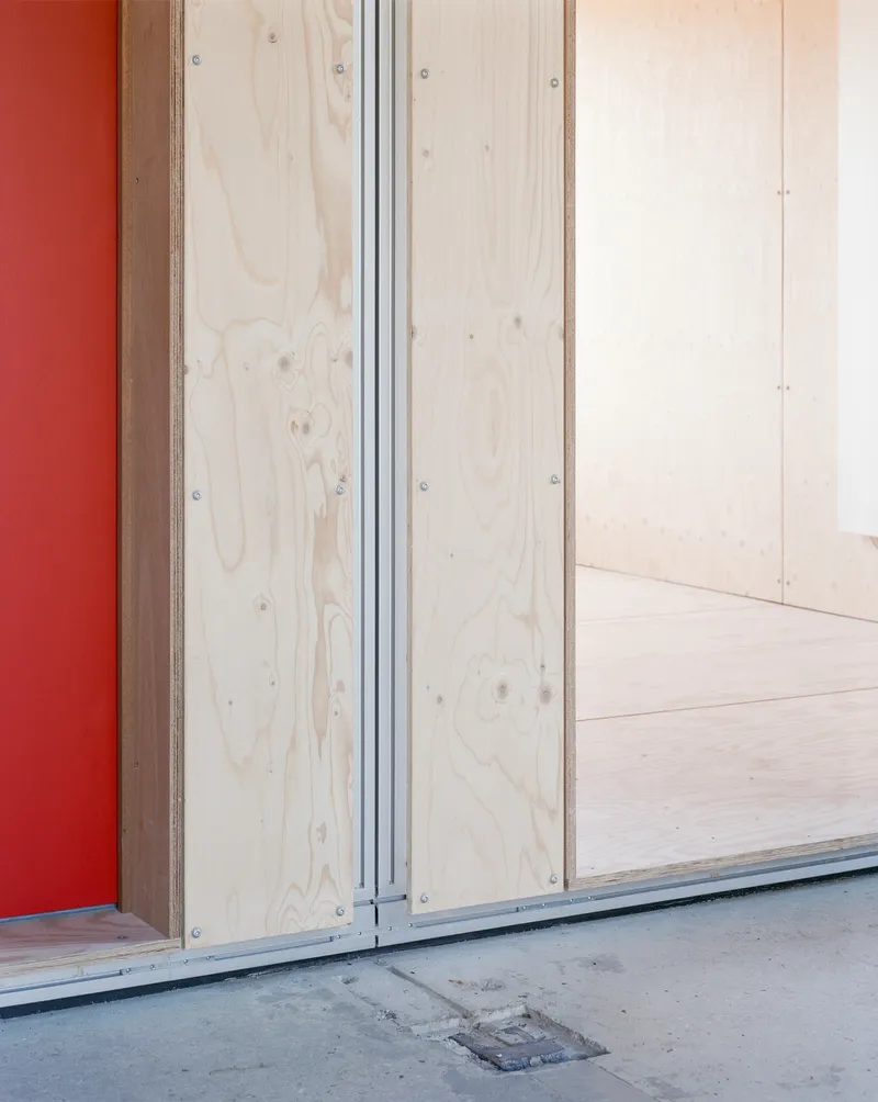 Detail of plywood door frame with exposed screws meeting grey concrete floor