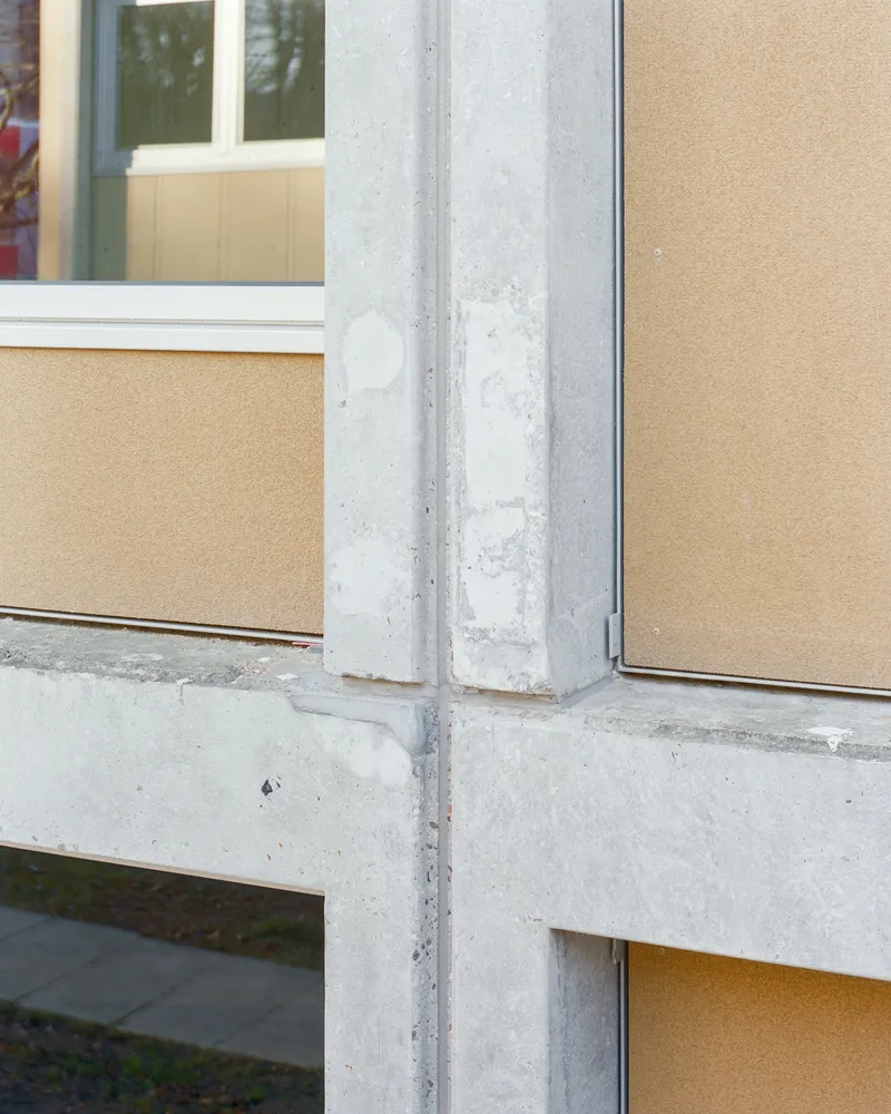 Close-up of the concrete structural column meeting pale wood-textured facade panels and glazed openings