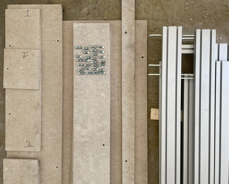 Material samples laid out showing pale board panels, metal fasteners, and white window frames