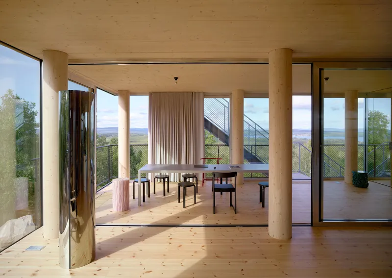Interior dining space with pale timber columns and plywood ceiling framing views of hills and lake