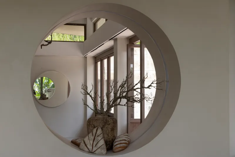 Interior view through circular wall opening revealing a second round aperture and natural light beyond