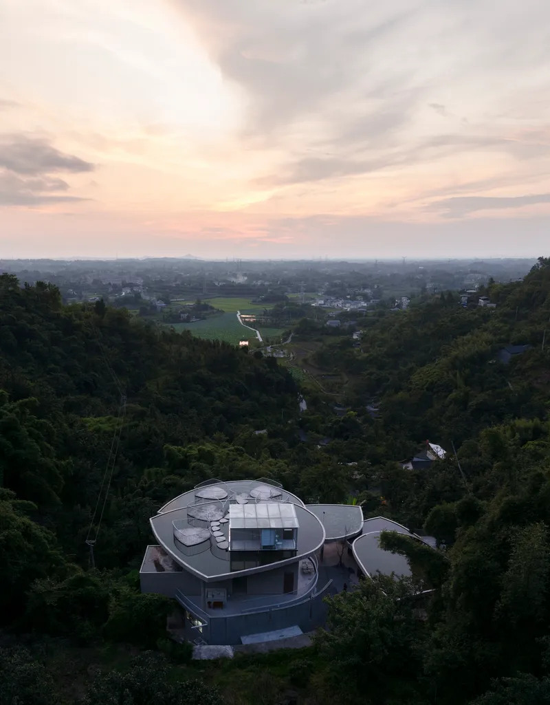 Aerial view of multi-lobed roof structure nestled in forested hillside at dusk
