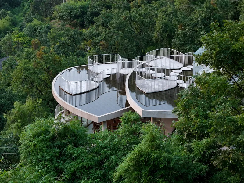 Elevated view of organic roof forms with vertical slat railings surrounded by dense forest canopy