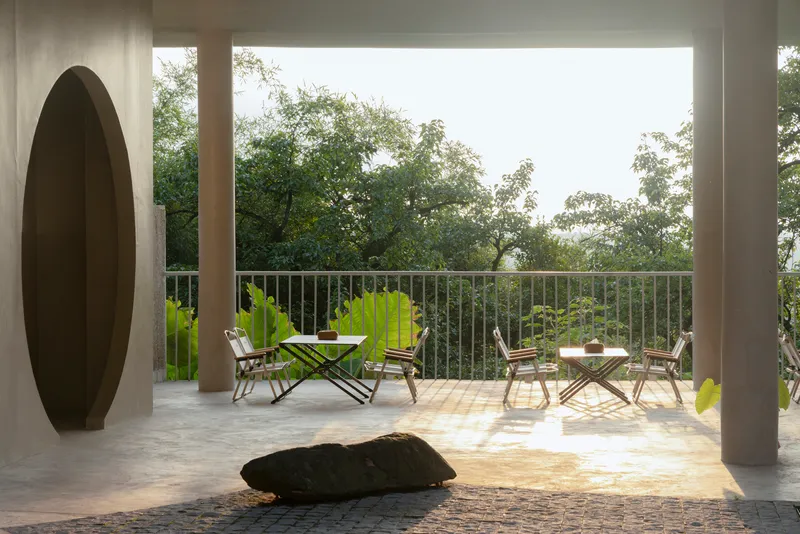 Covered terrace with cylindrical columns and metal railings framing outdoor furniture and tropical vegetation
