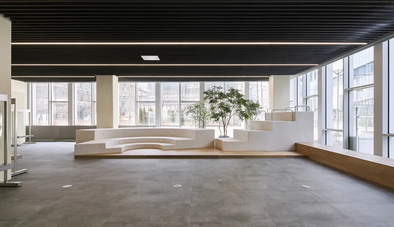 Curved white concrete seating plinth beside floor-to-ceiling windows under a black slatted ceiling