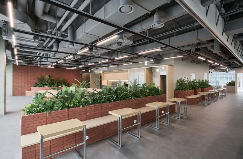 Rows of terracotta tile planters filled with greenery beneath a grid of exposed ductwork and linear lighting