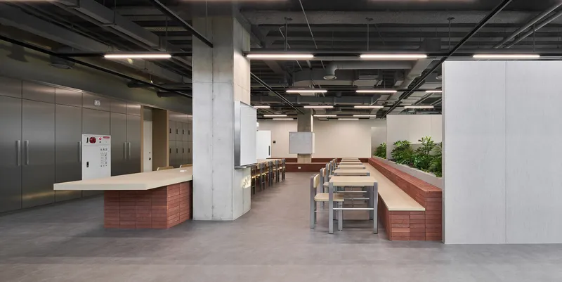 Central dining area with timber bench seating and concrete columns under exposed mechanical systems