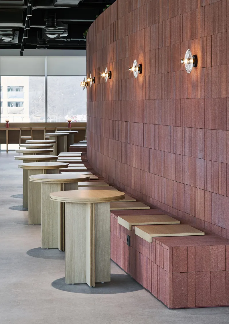 Row of light wood round tables along red textured block wall with mounted wall sconces