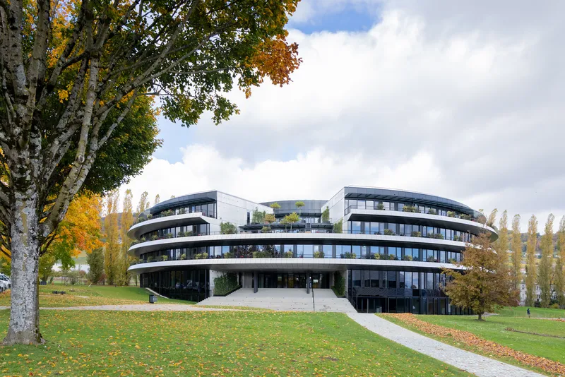 Curved facade with continuous balconies rising above a green lawn with autumn trees