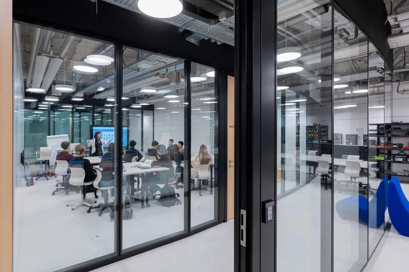 Glass-walled conference room with meeting in progress under exposed ceiling and pendant lights