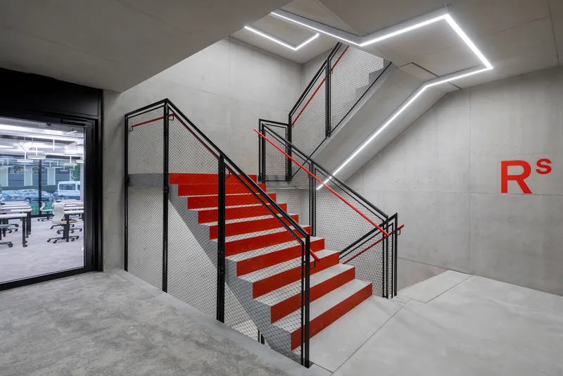 Red metal staircase with mesh guardrails and linear lighting recessed into concrete walls