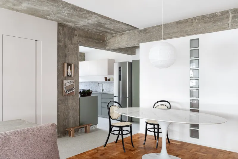 Open-plan living and dining area with exposed concrete beams and white cabinetry dividing the kitchen