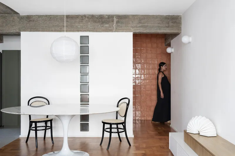 White partition wall with vertical glass block slot and woman in black dress passing through doorway