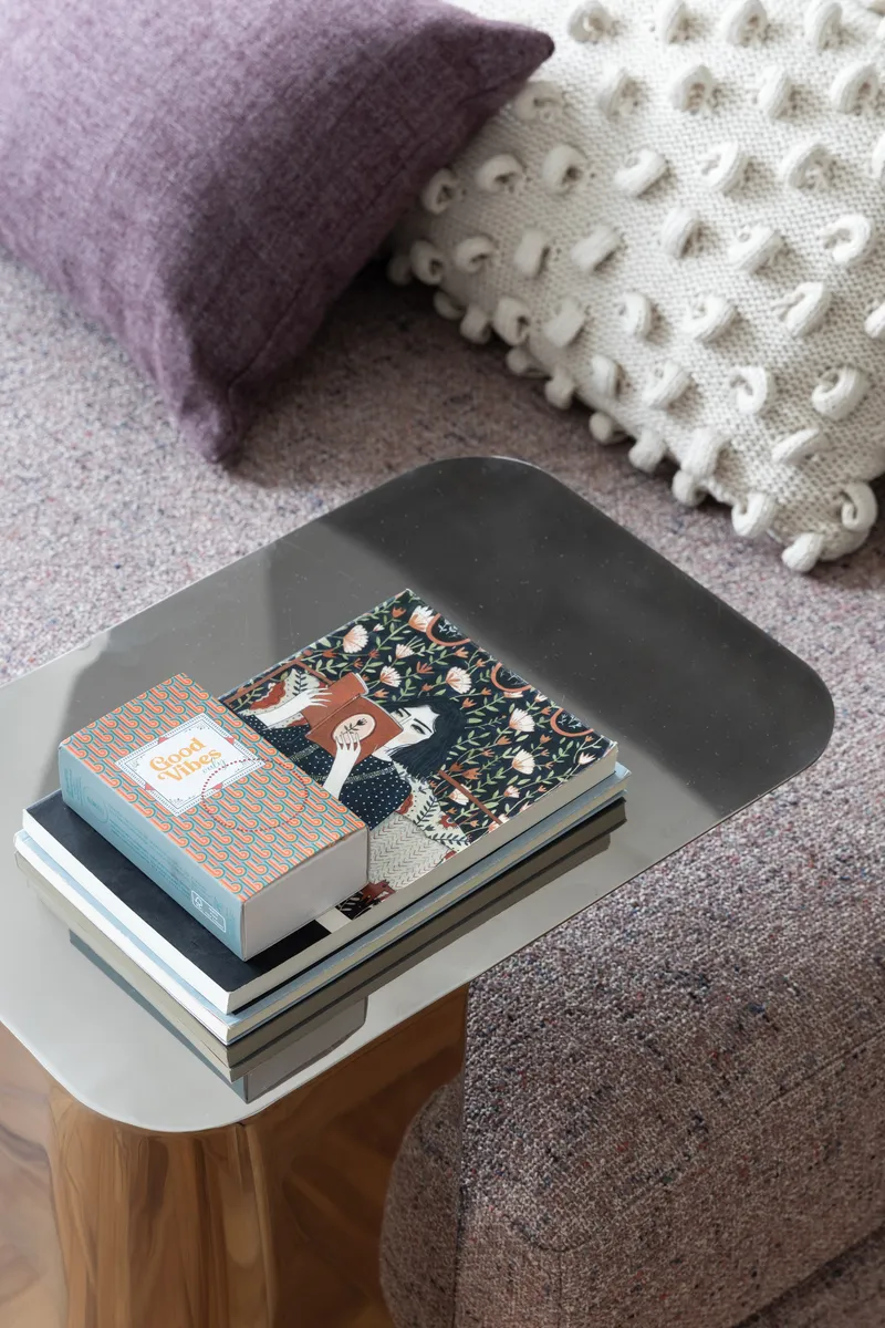 Gray curved side table with timber legs holding a stack of books beside textured cushions