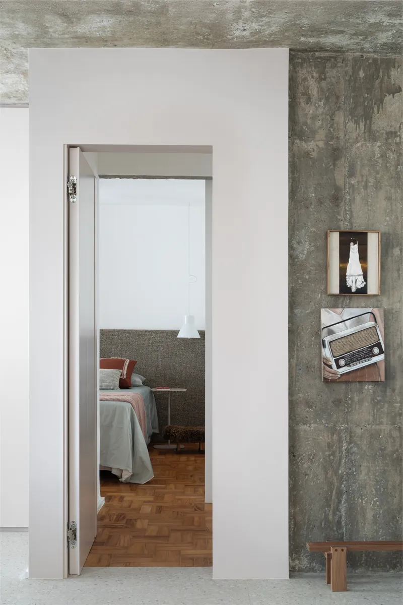 Open doorway revealing bedroom with parquet flooring beyond the exposed concrete and white plaster walls