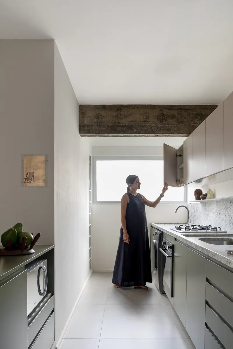 Galley kitchen with exposed concrete beam overhead and a woman opening an upper cabinet