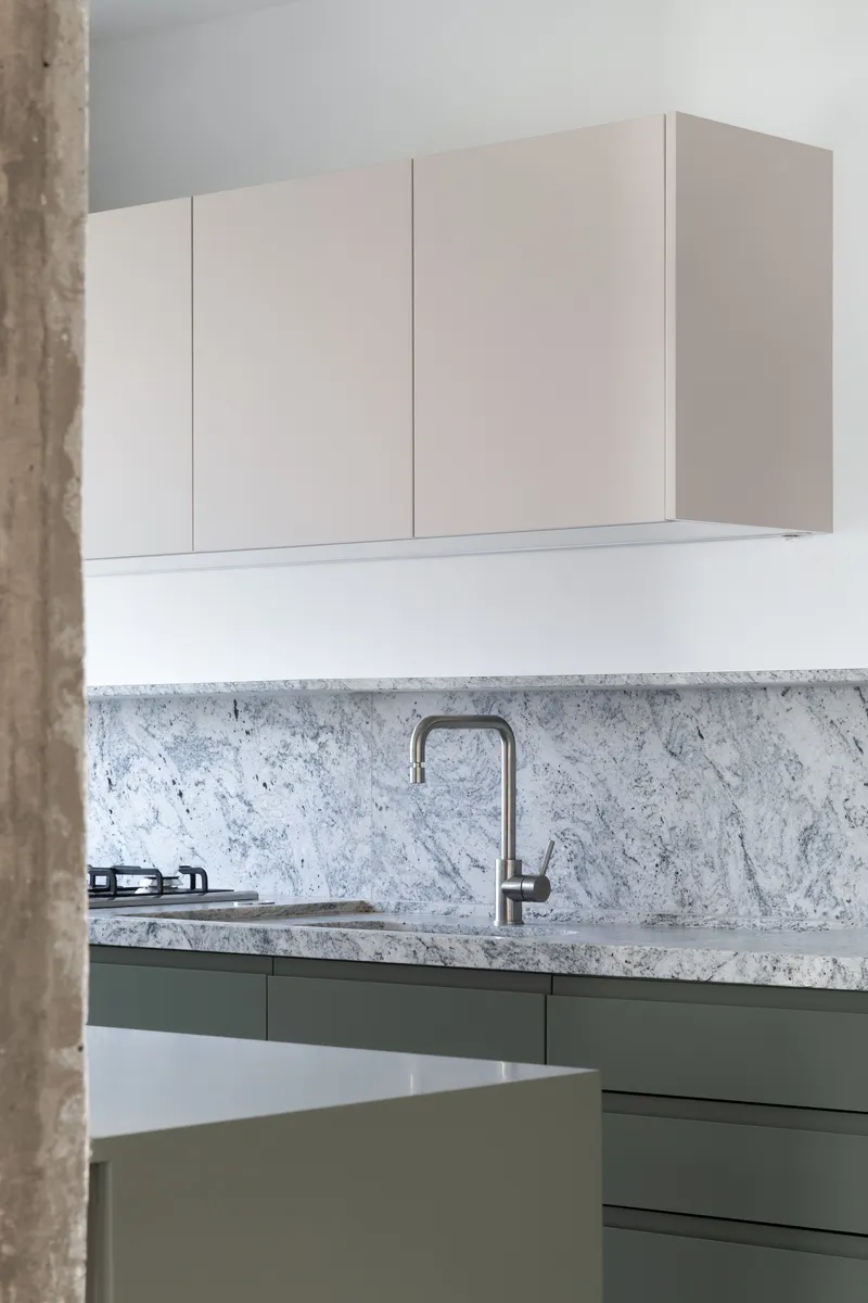 Kitchen counter detail showing white marble backsplash with sage green lower cabinets and steel faucet