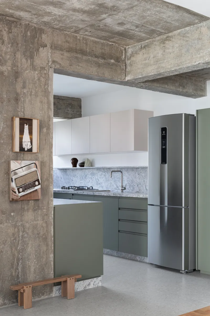 Kitchen view framed by concrete columns showing sage cabinetry and marble countertop with stainless refrigerator